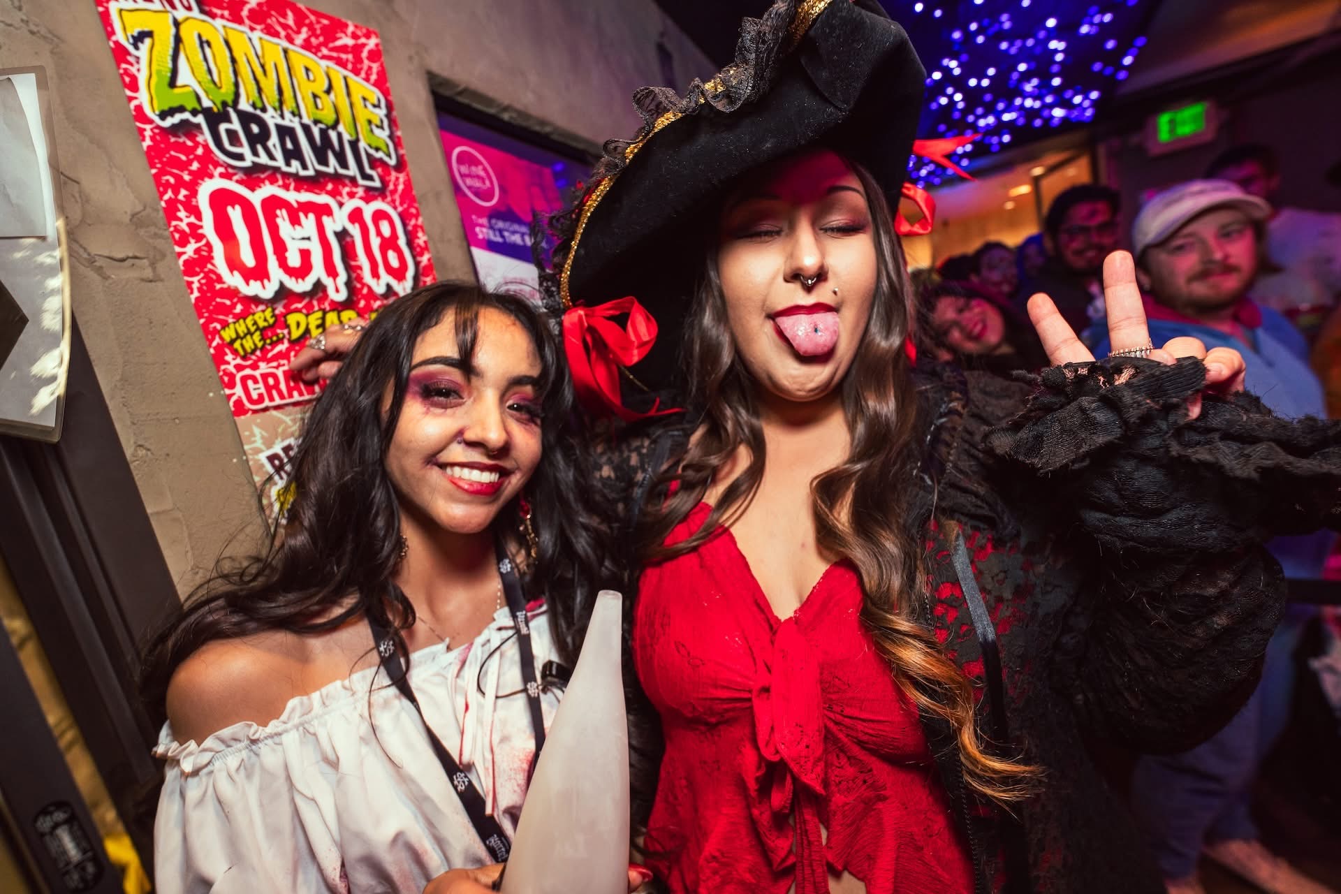 Two guests in Halloween costumes at Hookava during Zombie Crawl in front of Zombie Crawl Oct 18 poster